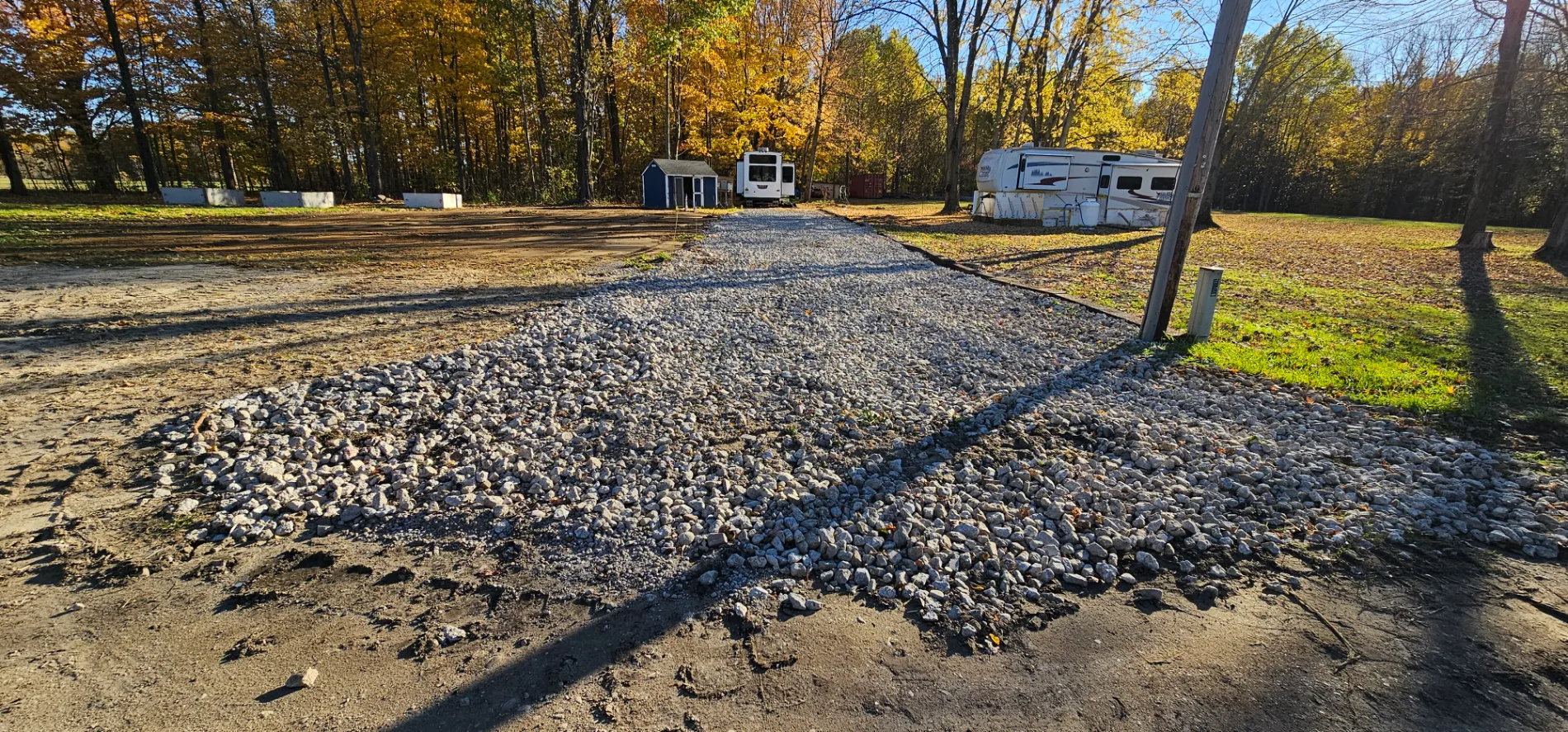 Newly installed gravel driveway on a cleared rural property with autumn trees